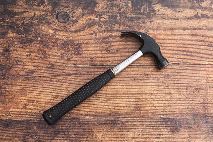 A black and silver metal hammer rests on a wooden board. The hammer has a black grip.