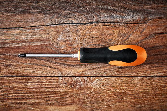 A black and orange handled Phillips screwdriver rests on a wooden background.