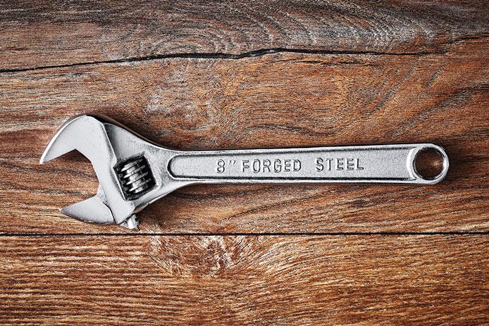 A standard-size silver wrench sits atop a wooden table.