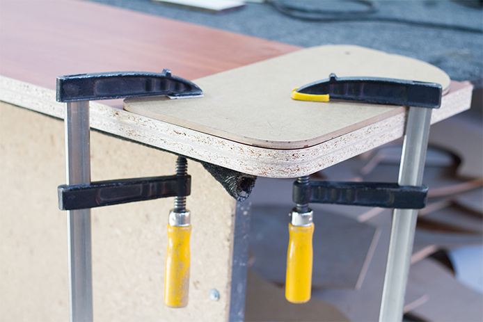 A board is shown with two black, yellow, and silver clamps holding I steadily in place.